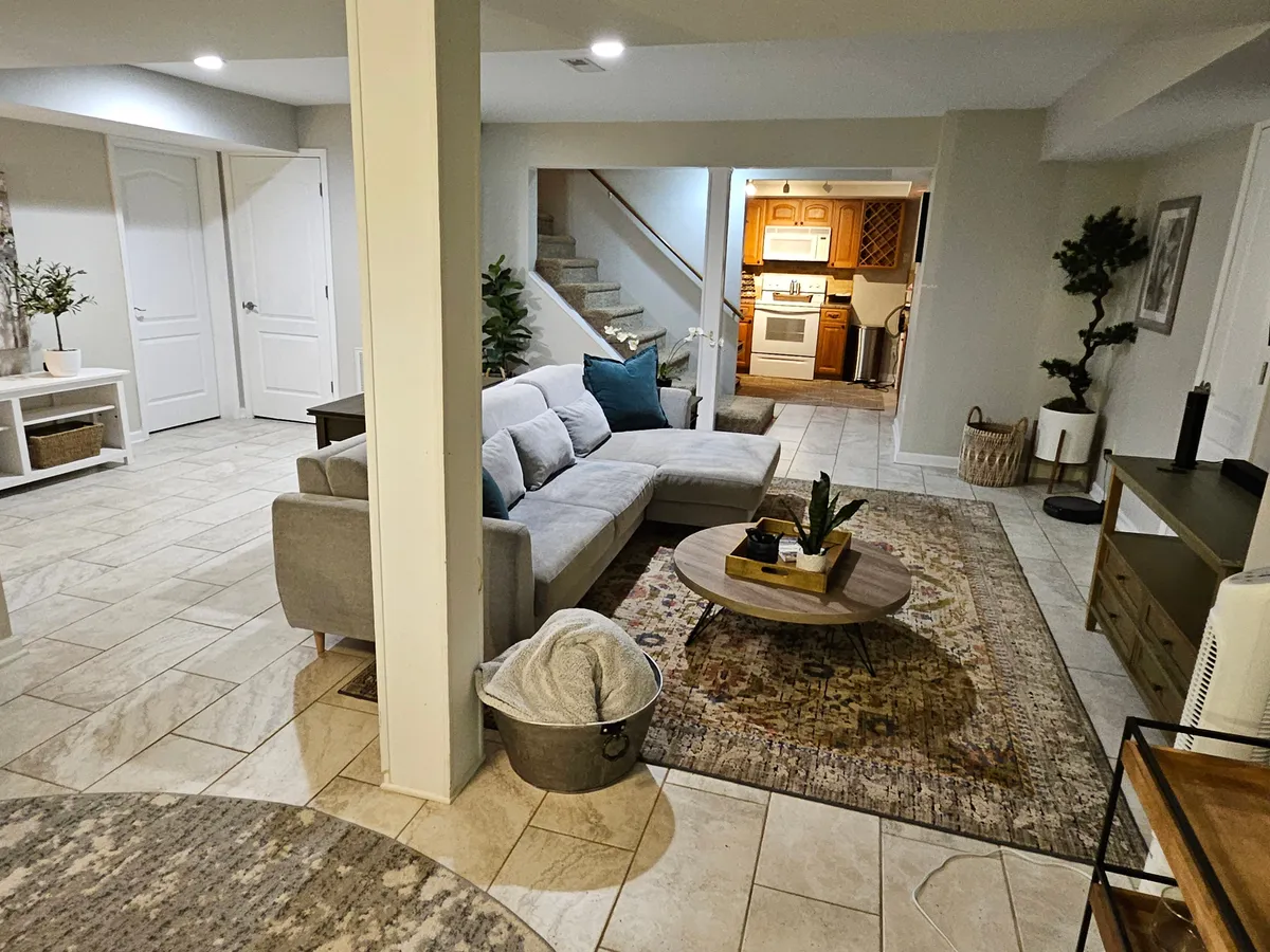 This view captures a broader perspective of the open-concept great room, with a sofa, coffee table, and area rug flowing toward a visible kitchen area and staircase. The arrangement is ideal for entertaining, relaxing, or even casual work sessions, highlighting the seamless transition between living and dining spaces.
