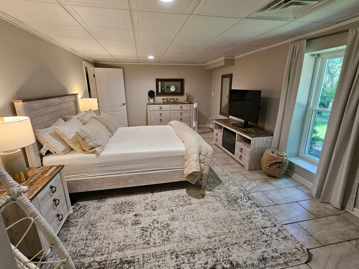 A serene bedroom scene shows a bed with neutral linens, a dresser adorned with decorative items, and a window bathed in soft natural light, creating an atmosphere of calm and tranquility—the perfect respite after a day exploring Mooresville or commuting for business.