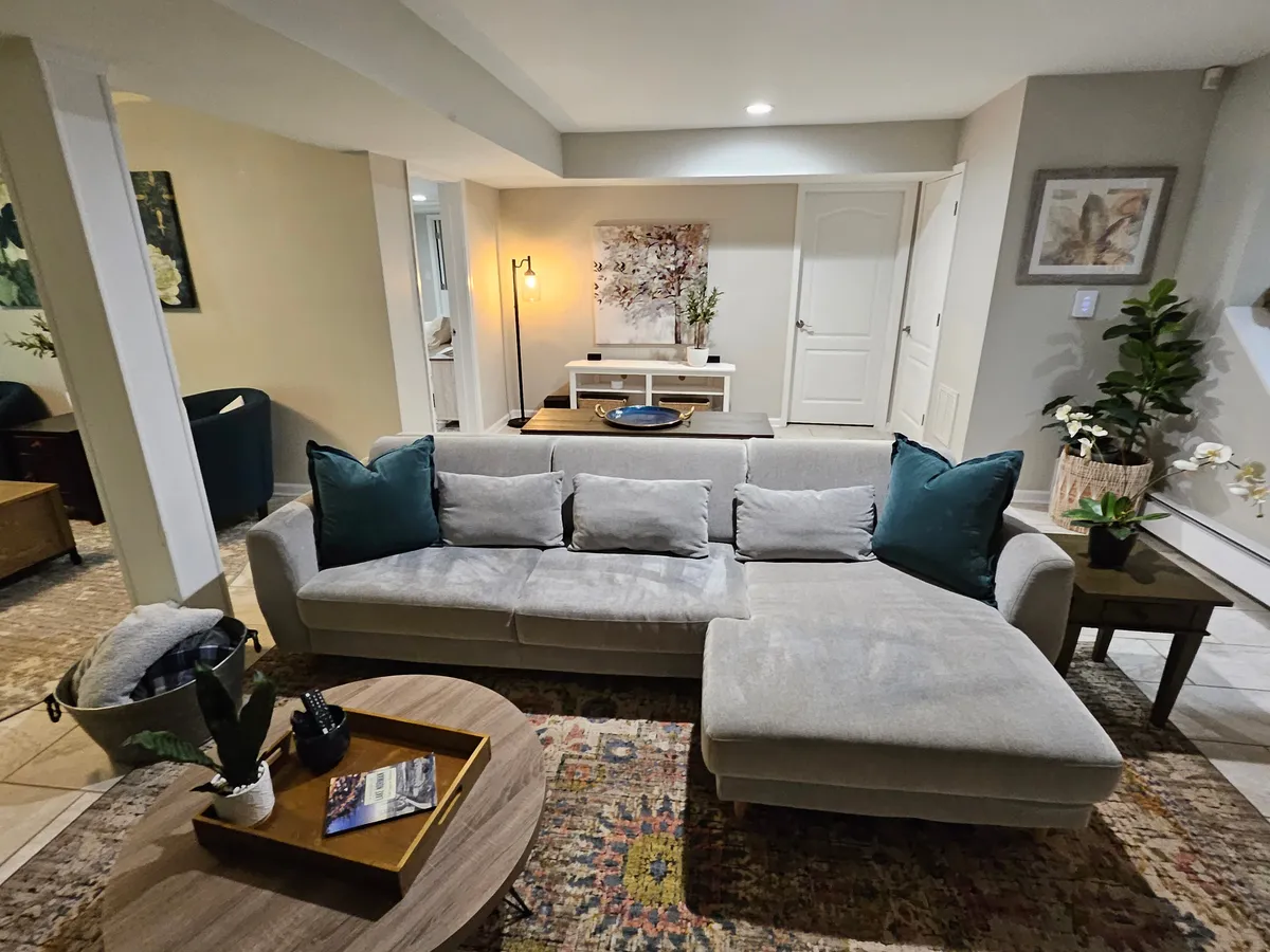A stylish living area with a comfortable sofa, coffee table, potted plants, and decorative artwork. The presence of greenery indoors echoes the garden theme, and the scene communicates relaxation and unwinding in a chic yet natural environment.