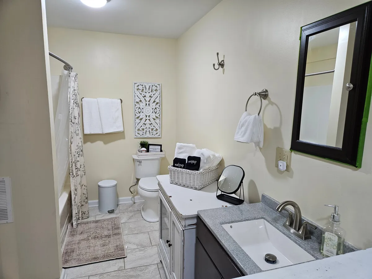 A bright, spa-like ensuite bath featuring a modern sink with a sleek faucet, decorative wall art, clean towels, and a basket of toiletries. The space exudes cleanliness and tranquility, perfect for pampering and self-care routines.