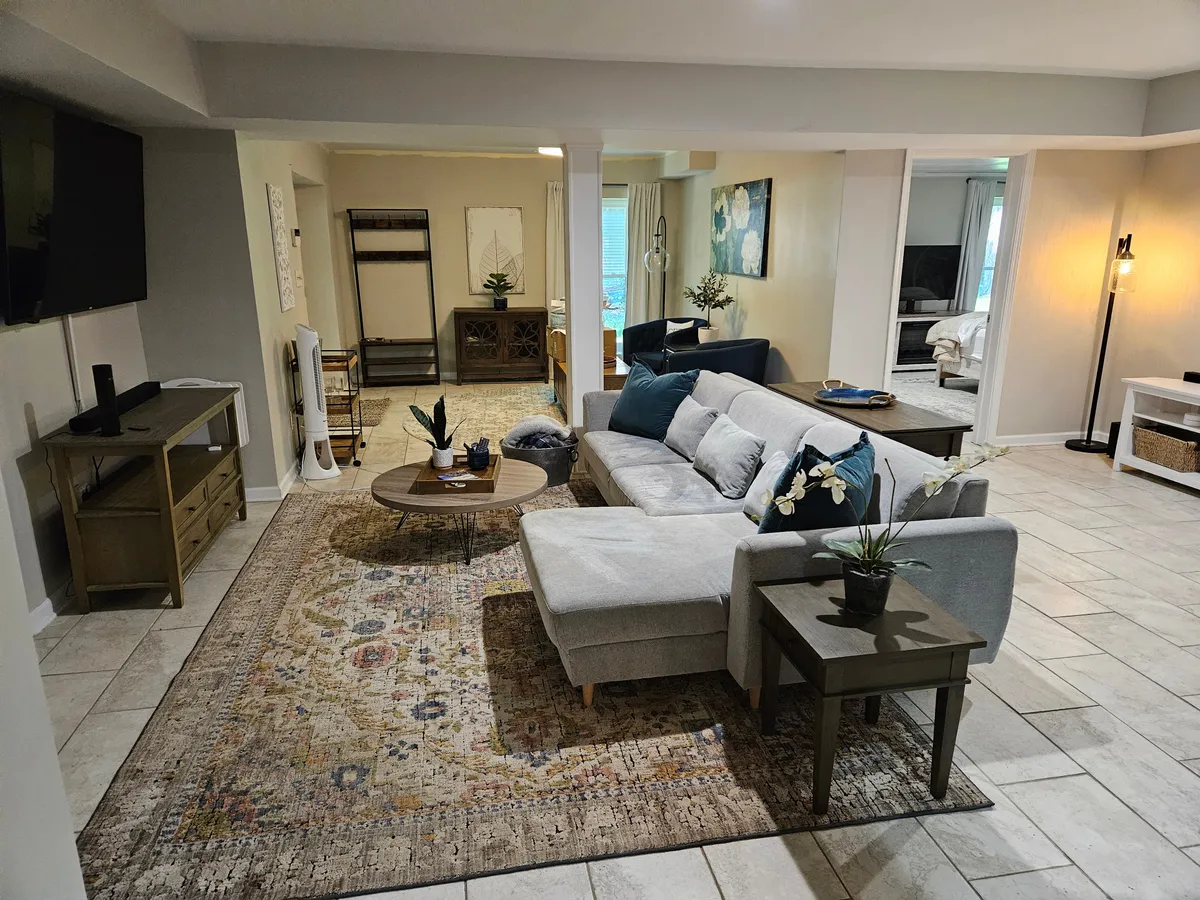 A comfortable and inviting great room scene, highlighting a sectional sofa, coffee table, decorative rug, and floor lamp. The arrangement encourages relaxation, reading, and socializing, with a TV for entertainment. The space feels open yet cozy, suggesting both solo downtime and lively gatherings.