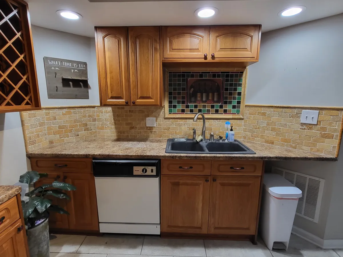 A warm, welcoming kitchen scene featuring rich wooden cabinets, a granite countertop, and a vibrant, colorful backsplash. The sink and ample workspace are visible, providing a sense of functionality and space for meal preparation. The environment feels inviting—ideal for hosting, cooking, and casual socializing.