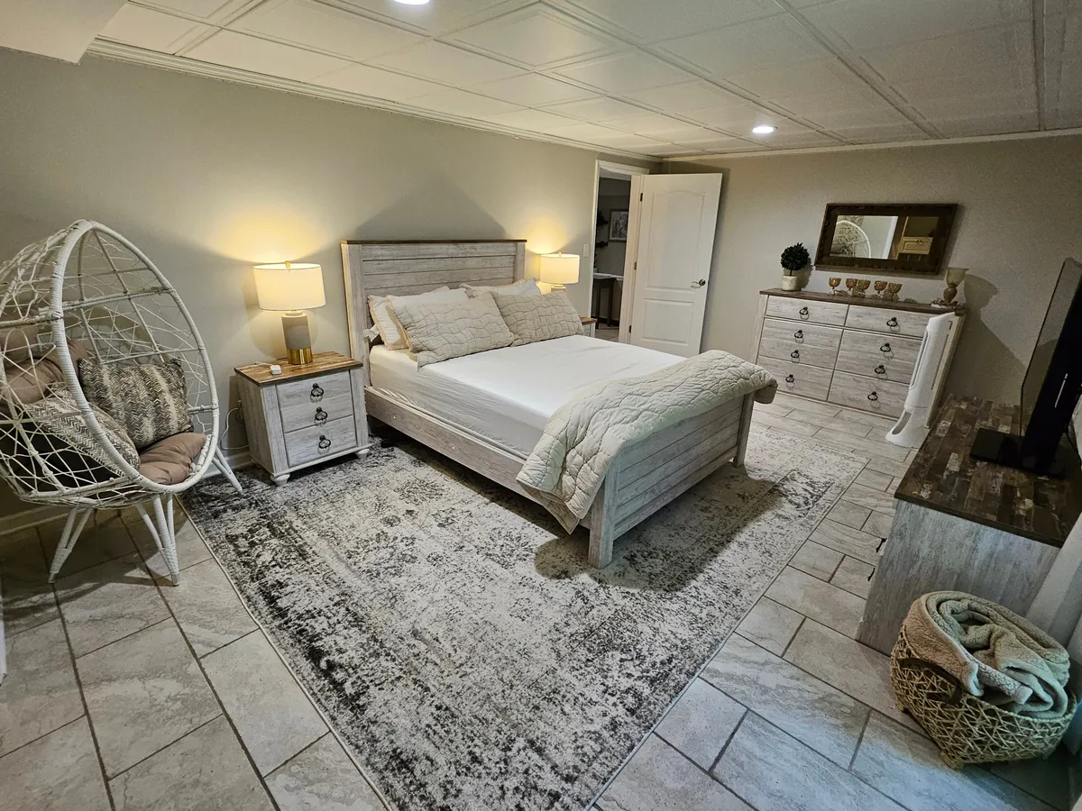This image features a comfortable bedroom with a bed, hanging chair, dresser, and TV unit. Natural light filters in, giving the space an inviting atmosphere that suggests a place to unwind and recharge. The hanging chair adds a unique touch, hinting at relaxation options beyond the ordinary.